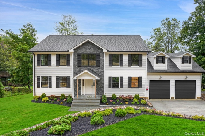 virtually staged Colonial home featuring a front lawn, driveway, a shingled roof, and a garage