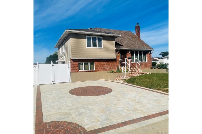 Split level home featuring brick siding, a chimney, a gate, and roof with shingles