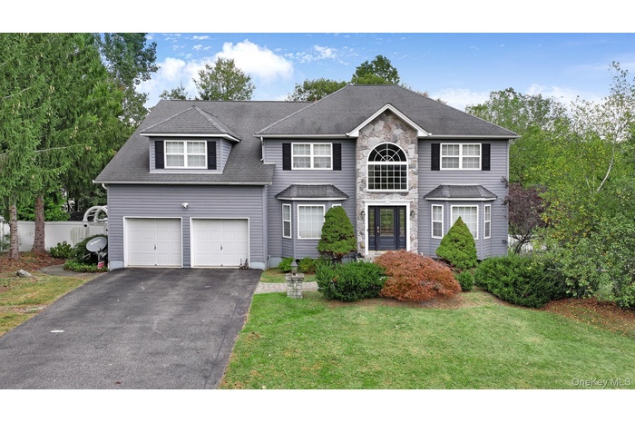 View of front of property featuring driveway, stone siding, a shingled roof, and a garage