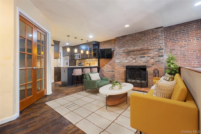 Living area with dark wood-style flooring, recessed lighting, a brick fireplace, and brick wall