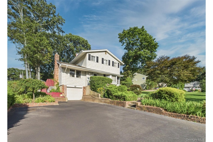 View of front of home featuring asphalt driveway, a chimney, an attached garage, and brick siding