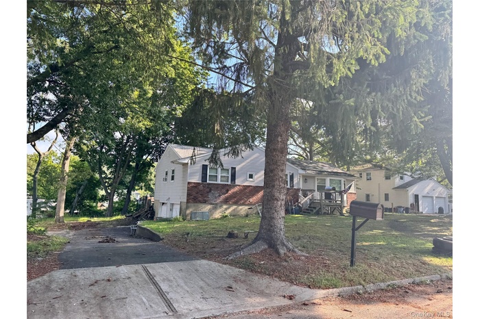 View of front of property with driveway, a front lawn, a deck, brick siding, and view of wooded area