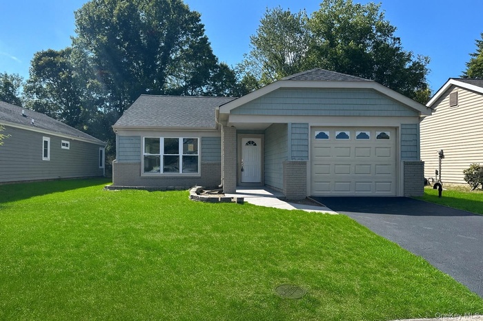 View of front of property with a front lawn, driveway, a garage, brick siding, and a shingled roof