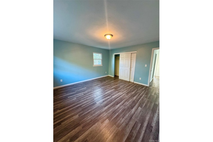 Unfurnished bedroom with a closet, dark wood-style floors, and a textured ceiling