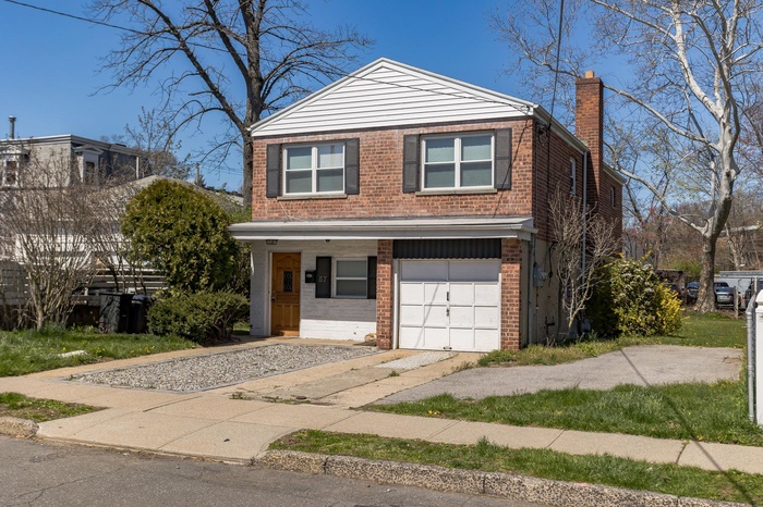 View of front of house with brick siding, a chimney, an attached garage, and driveway