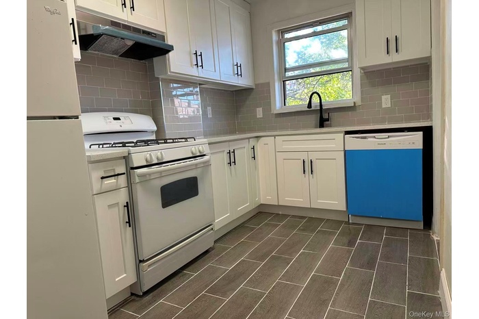 Kitchen featuring white appliances, under cabinet range hood, white cabinets, backsplash.