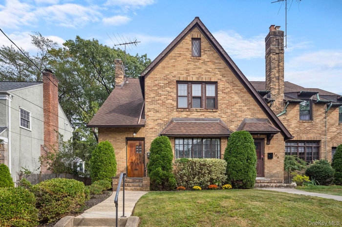 Tudor home with brick siding, a chimney, entry steps, and a shingled roof
