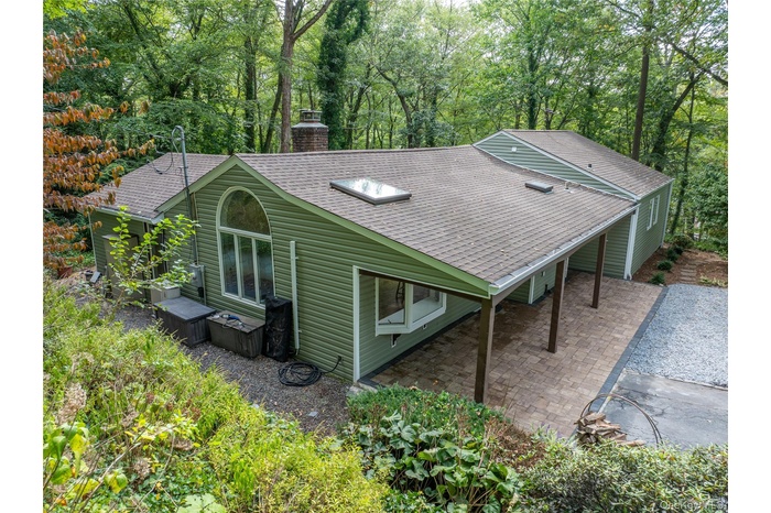 Rear view of property featuring a shingled roof, a chimney, view of wooded area, and a patio