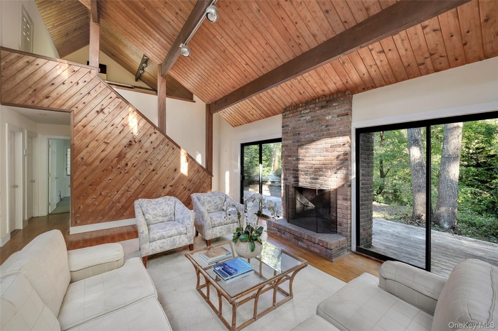 Living room featuring wood finished floors, high vaulted ceiling, a wood ceiling with exposed beams, and a brick fireplace