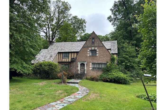 Tudor-style house featuring a high end roof, a front yard, brick siding, and view of scattered trees