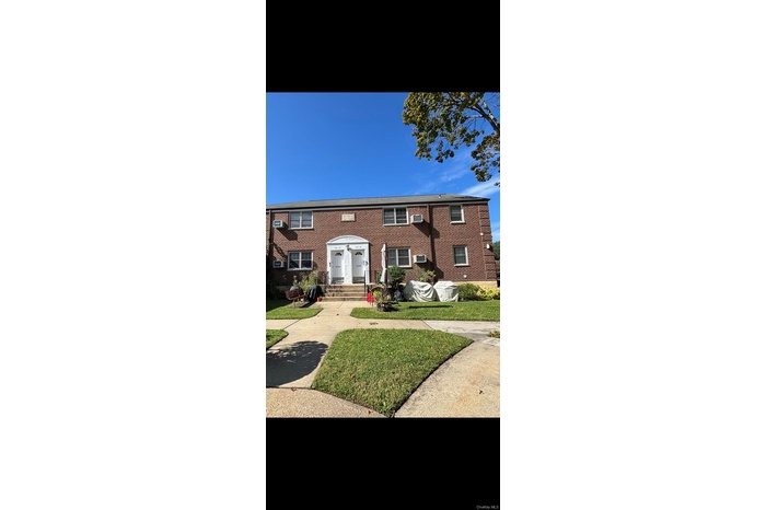 View of front of house with a front lawn, brick siding, and a wall unit AC