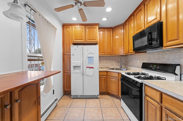 Kitchen with range with gas stovetop, white fridge with ice dispenser, light tile patterned floors, a baseboard radiator, and brown cabinets