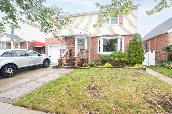 View of front of house featuring a front yard, brick siding, concrete driveway, a garage, and a gate