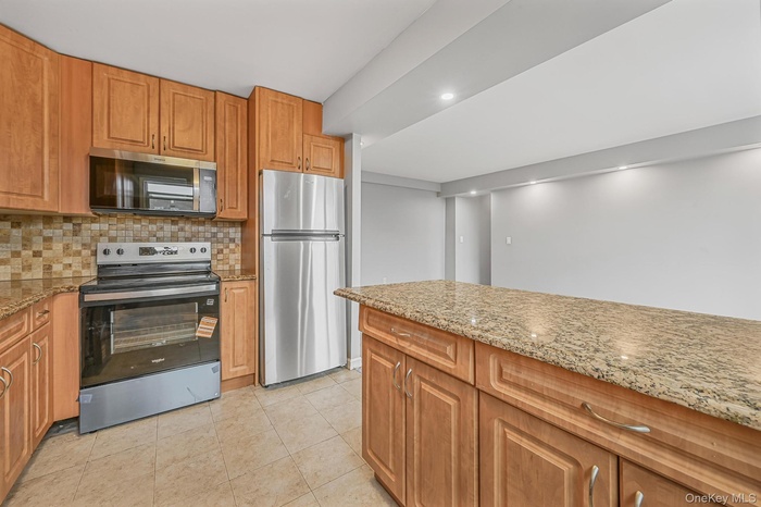 Kitchen featuring stainless steel appliances, light stone counters, tasteful backsplash, brown cabinets, and recessed lighting