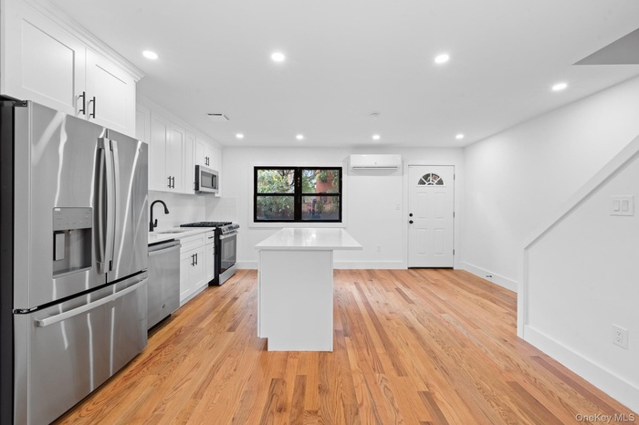 Kitchen with stainless steel appliances, white cabinets, a center island, recessed lighting, and light stone countertops