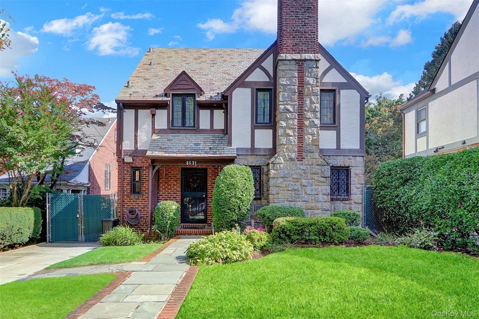 Tudor home featuring a high end roof, a gate, stone siding, a chimney, and stucco siding