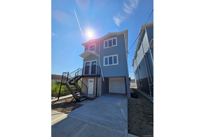 Beach home featuring stairway, concrete driveway, a garage, and a balcony