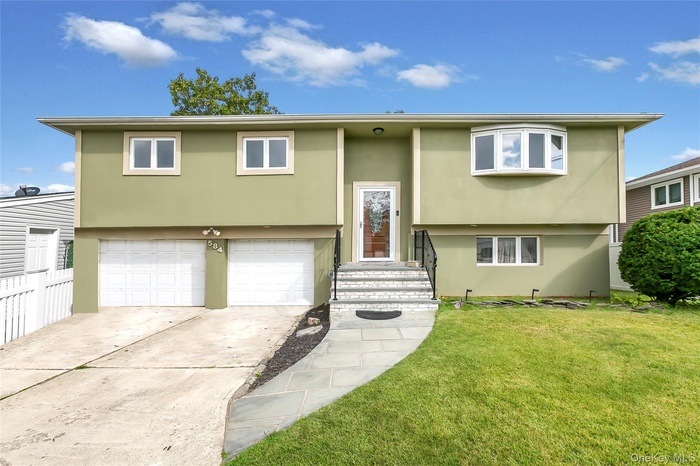 Bi-level home featuring stucco siding, a front lawn, concrete driveway, and a garage