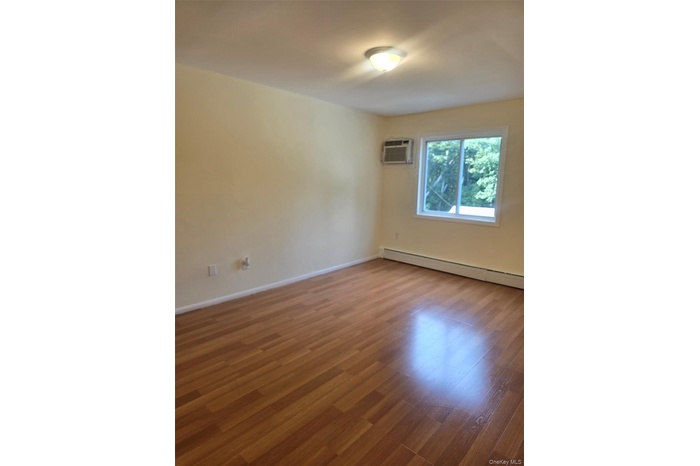 Empty room featuring wood finished floors, a baseboard radiator, and an AC wall unit