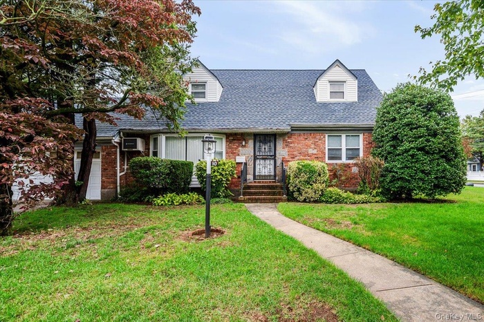 New england style home featuring brick siding, a front yard, and a shingled roof