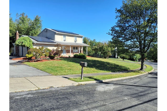 View of front facade featuring roof mounted solar panels, a front yard, covered porch, and a chimney