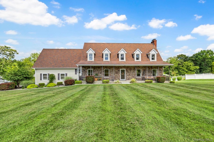 Cape cod house with a chimney, covered porch, and stone siding