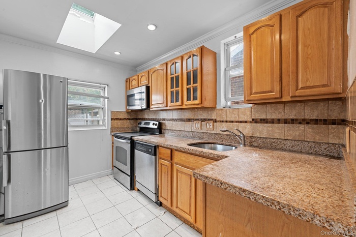 Kitchen with ornamental molding, a skylight, appliances with stainless steel finishes, tasteful backsplash, and light tile patterned flooring