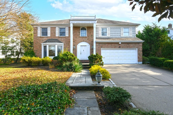 Greek revival house with driveway, a garage, and brick siding