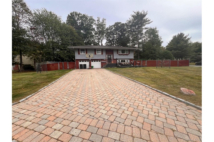 Split foyer home with decorative driveway, an attached garage, and view of wooded area