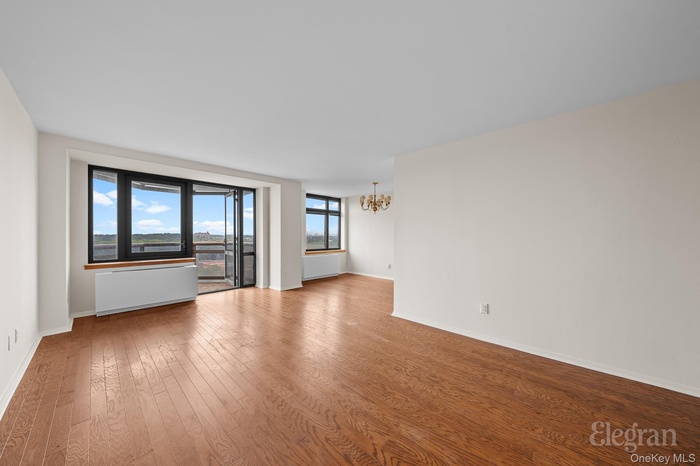 Empty room with wood finished floors, radiator, and a chandelier