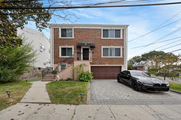 View of front of home with decorative driveway, a front yard, brick siding, and stairway