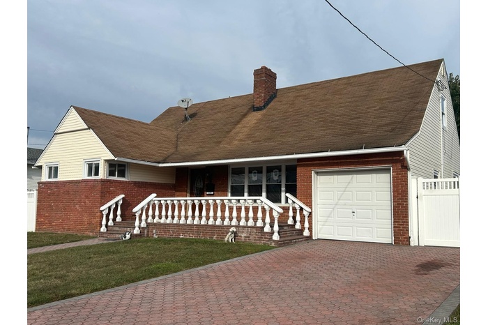 View of front facade with brick siding, a chimney, decorative driveway, and a front yard