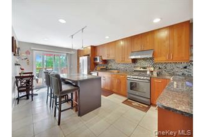 Kitchen with a kitchen island, a kitchen breakfast bar, decorative backsplash, stainless steel range, and brown cabinetry