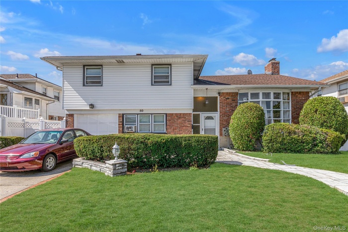 Tri-level home with brick siding, a front lawn, a chimney, and asphalt driveway