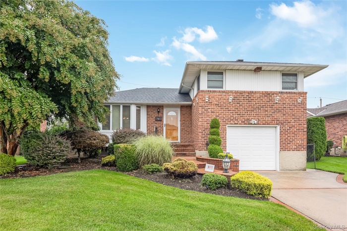 Split level home with concrete driveway, a garage, brick and vinyl siding, and a front yard