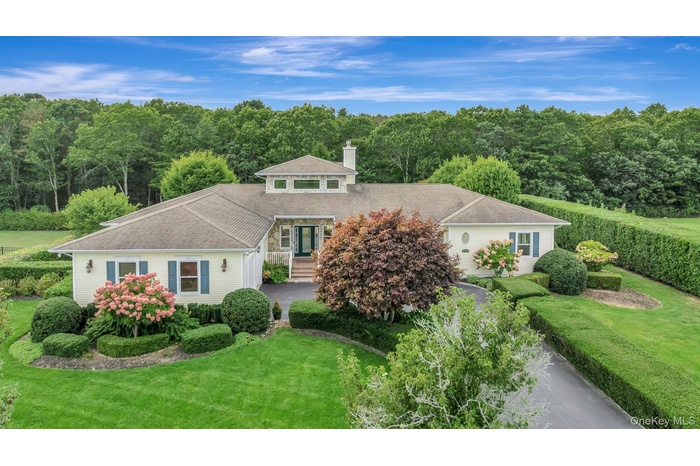 View of front of house featuring roof with shingles, a forest view, a chimney, and a front lawn