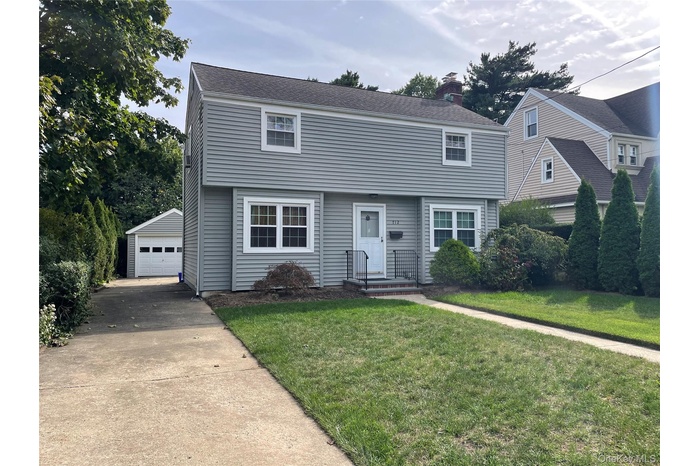 Colonial-style house with a front lawn, a chimney, concrete driveway, an outdoor structure, and a detached garage