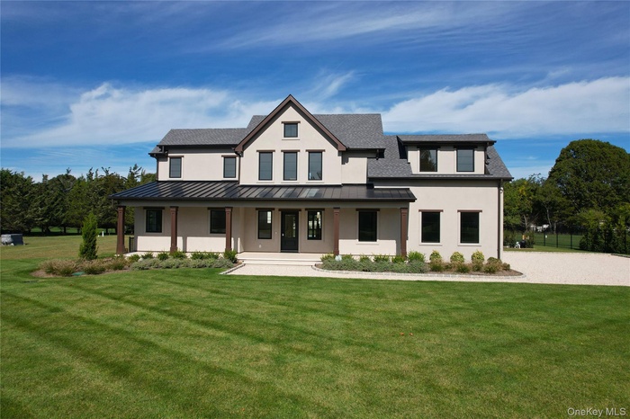 Modern farmhouse style home with a porch, a front lawn, stucco siding, and a standing seam roof