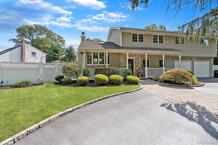 Traditional-style home featuring asphalt driveway, covered porch, a chimney, stone siding, and an attached garage
