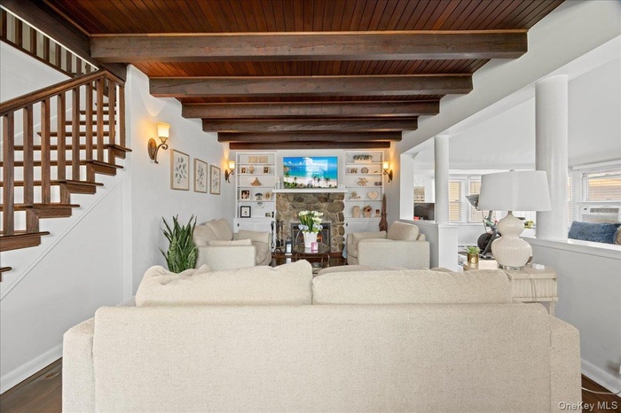 Living room with dark wood-style flooring, stairs, a stone fireplace, and a wooden ceiling with exposed beams