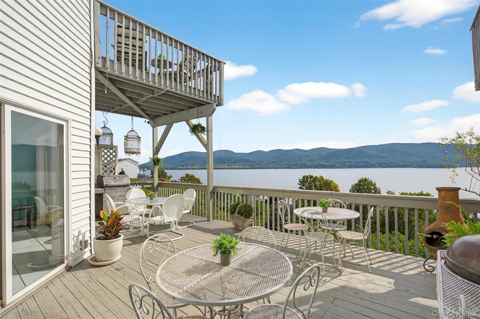 Wooden terrace featuring outdoor dining area, a water and mountain view, and a grill