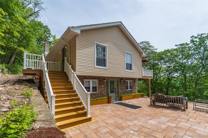 Side view of property with a patio area, stairs, stone siding, and a balcony
