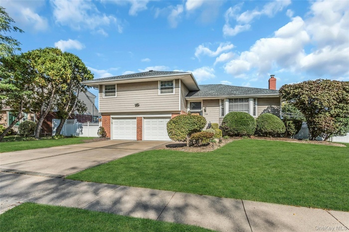 Tri-level home featuring brick siding, an attached garage, concrete driveway, and a chimney