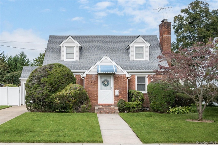 Cape cod house featuring brick siding, a shingled roof, and a chimney