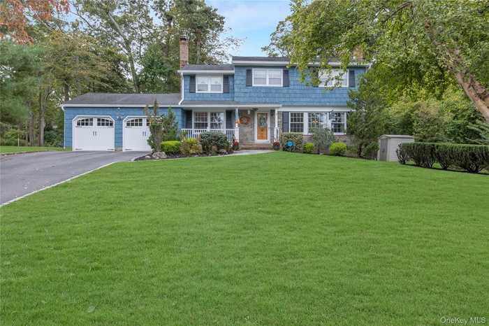 View of front of home with a chimney, covered porch, a garage, a front lawn, and driveway