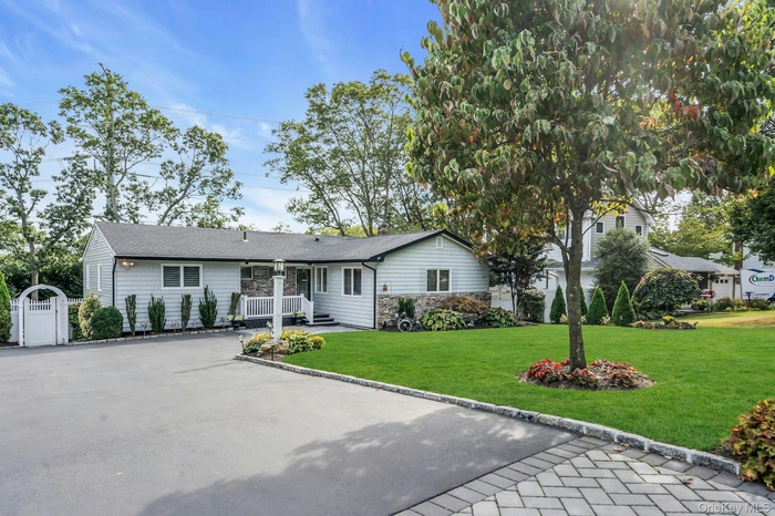 Ranch-style home featuring a front lawn, stone siding, a shingled roof, asphalt driveway, and a gate