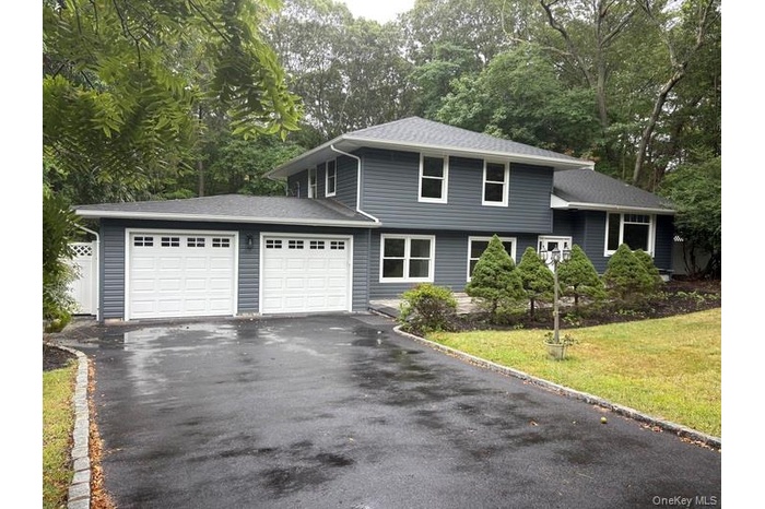 Tri-level home with an attached garage, view of wooded area, driveway, and a front yard