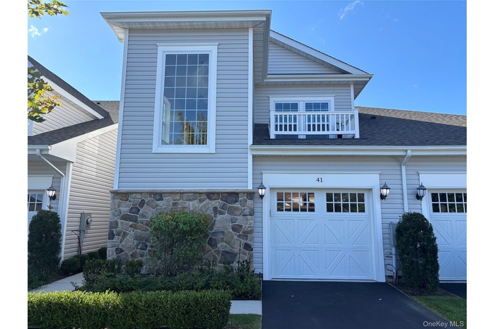 View of front of house featuring a balcony, a garage, driveway, and a shingled roof