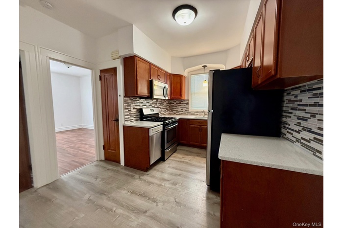 Kitchen featuring light wood finished floors, appliances with stainless steel finishes, backsplash, hanging light fixtures, and brown cabinetry