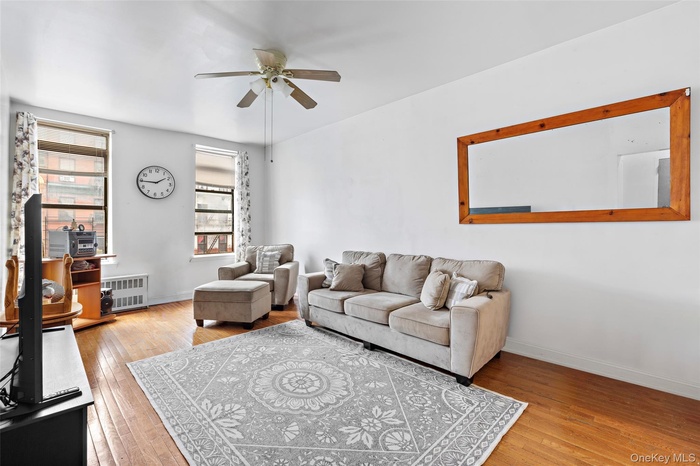 Living area with light wood finished floors, a ceiling fan, and radiator